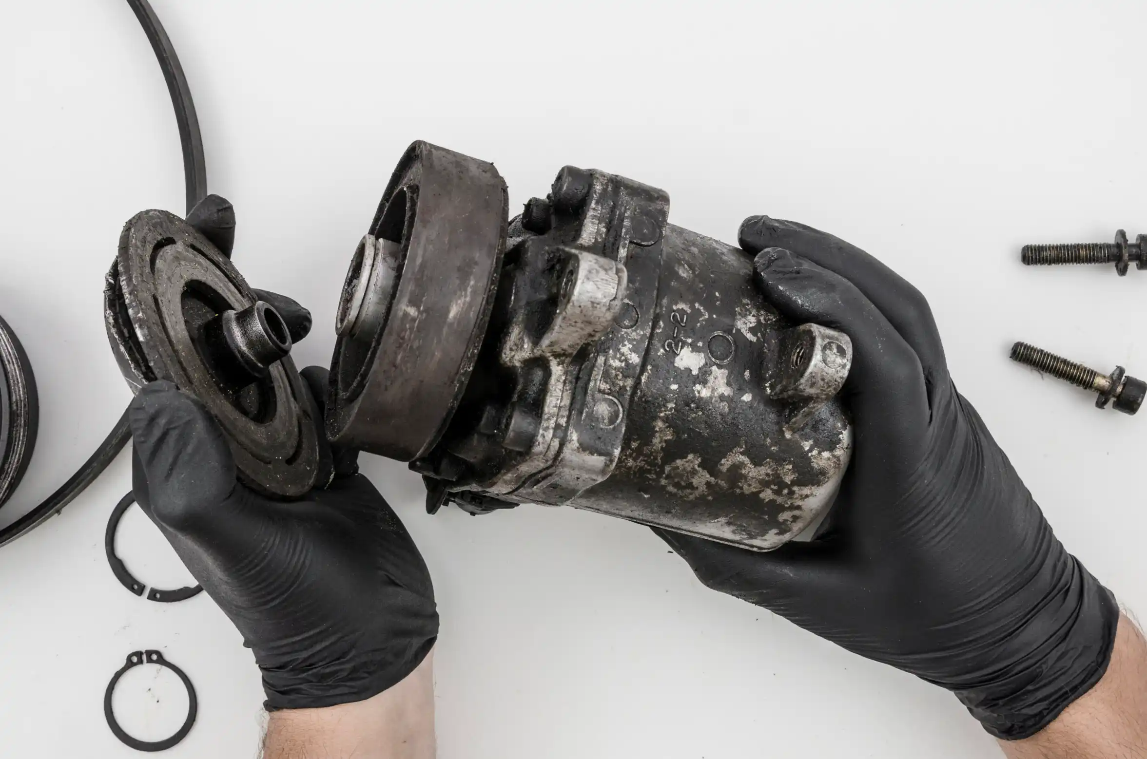 Mechanic in black gloves disassembling a worn car AC compressor part for catalytic converter scrap recycling in Sydney
